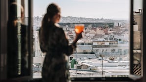 Una persona sosteniendo una bebida junto a una ventana con vistas a un paisaje urbano.