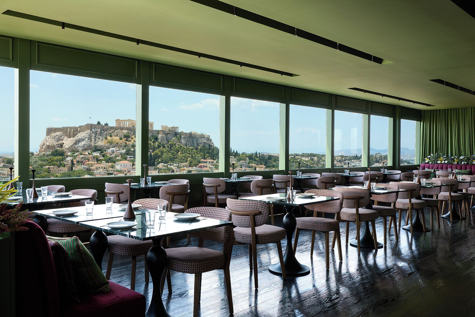 A restaurant with tables and chairs arranged for dining, large windows offering a view of a historic cityscape.