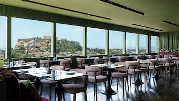 A restaurant with tables and chairs arranged for dining, large windows offering a view of a historic cityscape.
