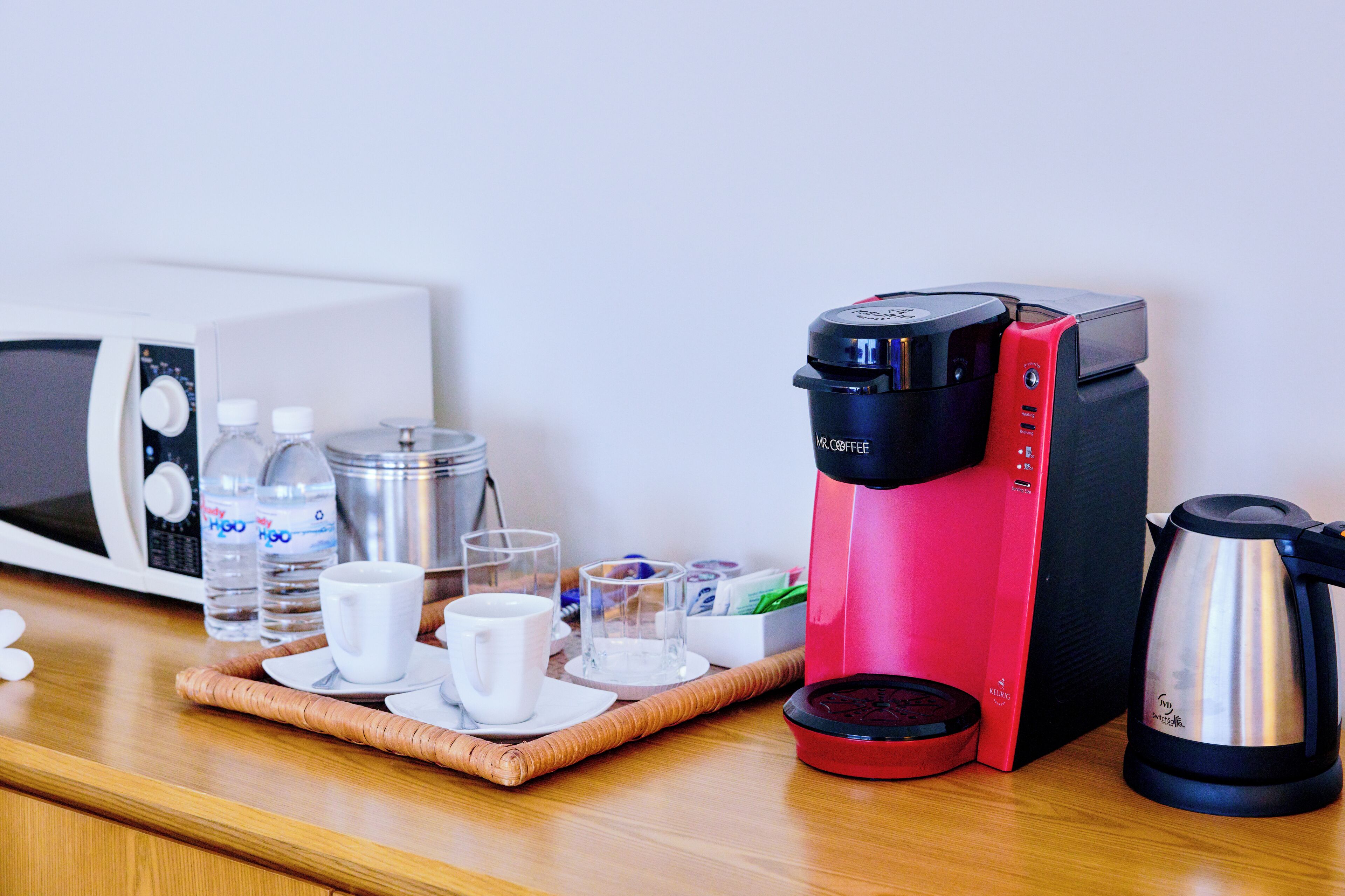 A coffee maker, water bottles, cups, and a kettle on a table.
