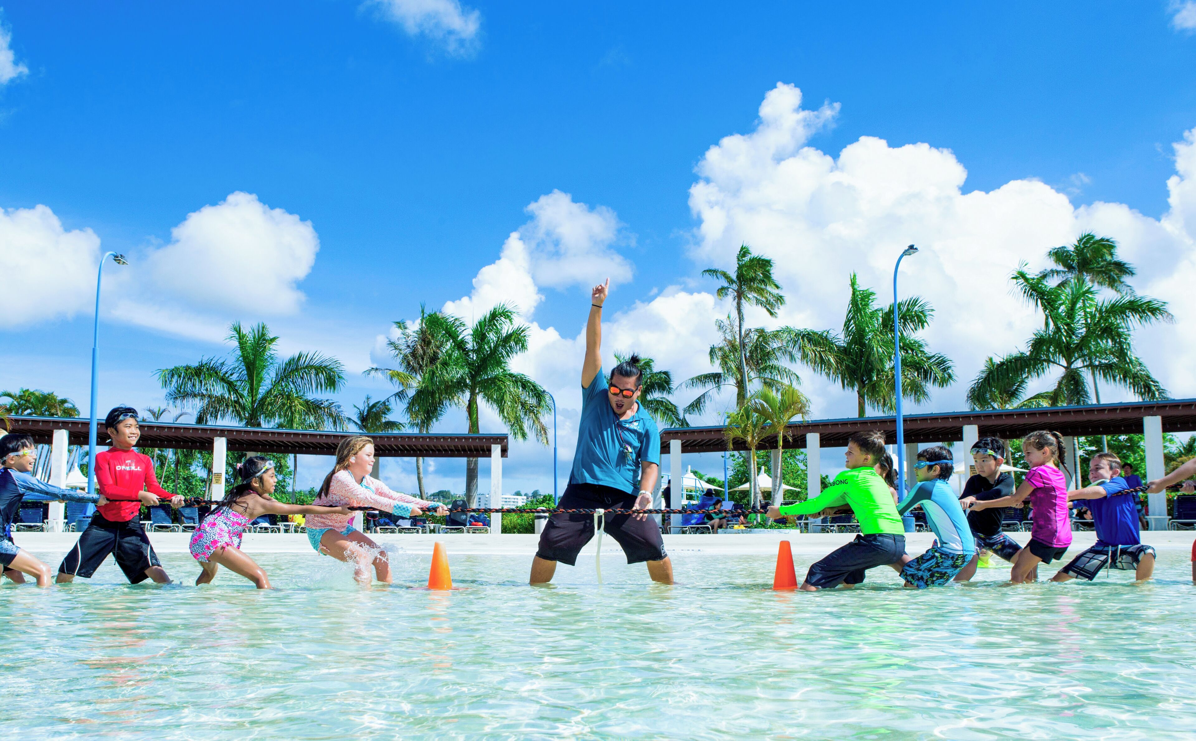 A group of people in a water activity, with clear skies and palm trees in the background.