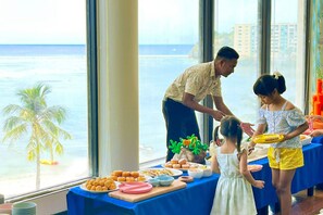 A dining area with a view of the ocean, a table with food, and a person serving food.