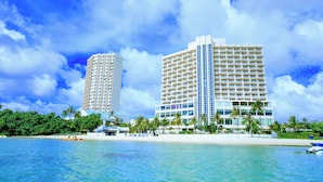 A beachfront hotel with multiple floors, a sandy beach, and palm trees.