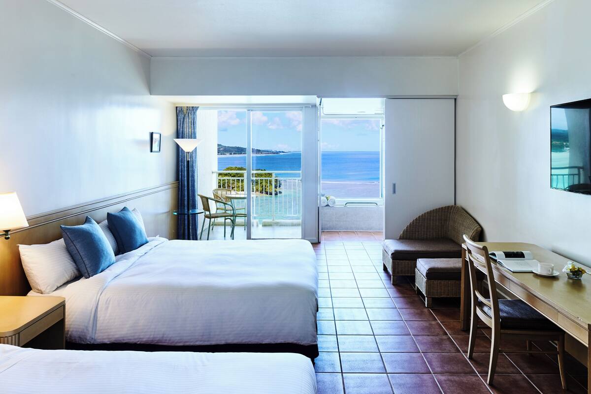 A hotel room with a bed, a desk, and a view of the ocean.