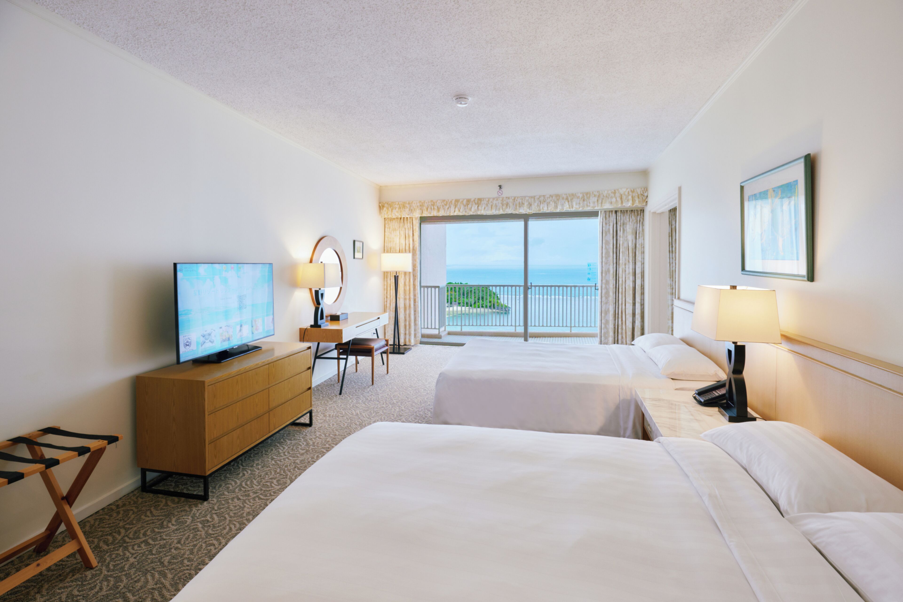 Habitación de hotel con dos camas, un escritorio, un televisor y un balcón con vistas.