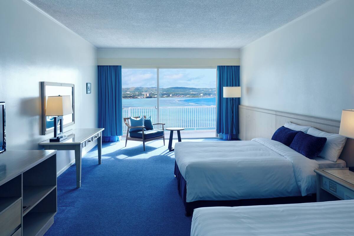 A hotel room with a large bed, a desk, a chair, and a view of the sea.