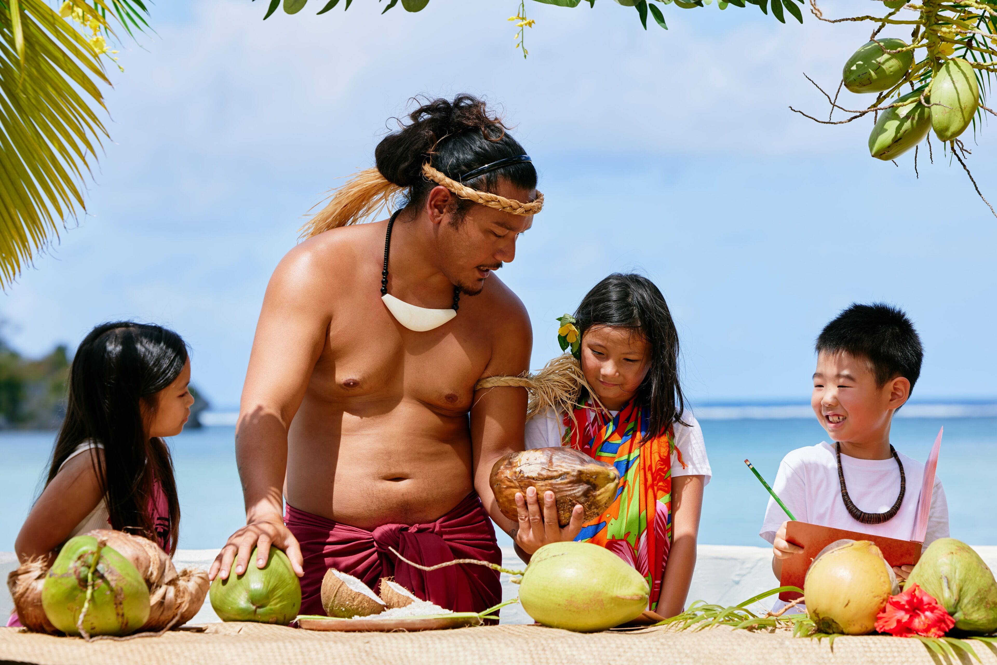 A group of people on a beach with coconuts and a palm tree.
