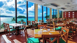 A restaurant with tables and chairs, large windows, and a view of the sea.