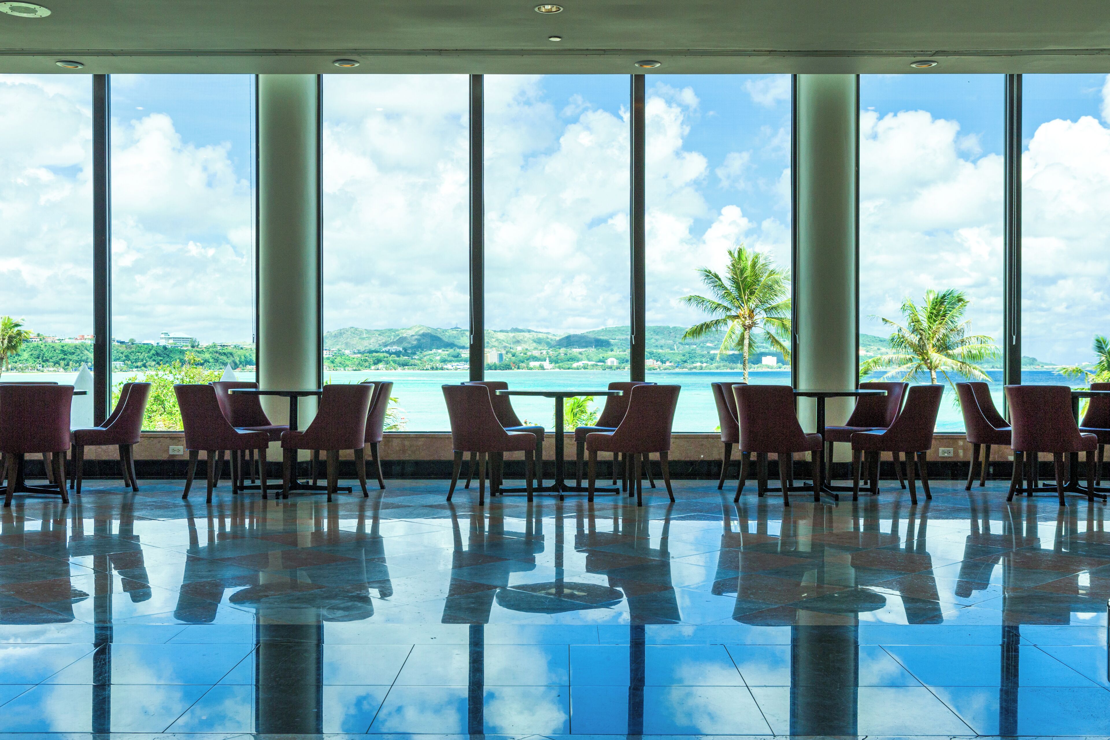 A spacious indoor area with large windows, reflective floor, and rows of chairs.