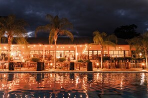 A hotel with outdoor seating, a swimming pool, and palm trees.