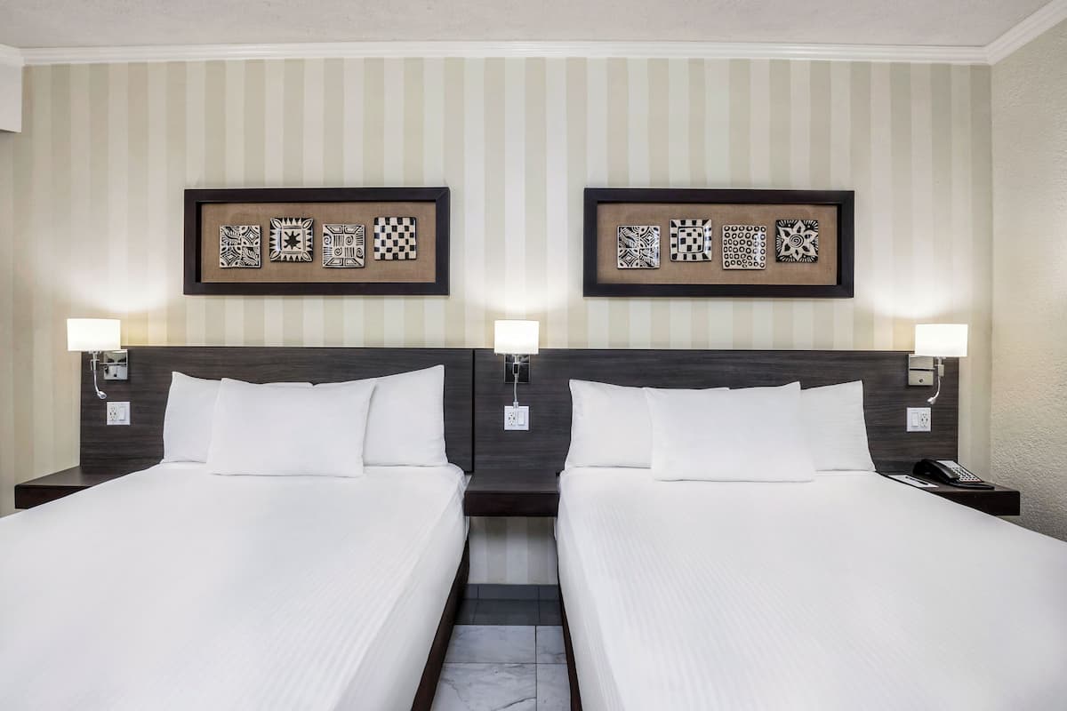 A hotel room with two beds, a striped wall, and framed artwork above each bed.