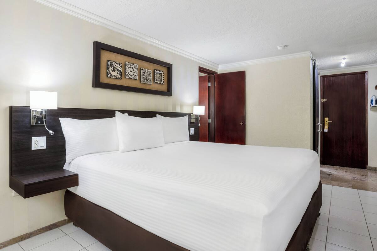 A hotel room with a large bed, a nightstand, a wall-mounted artwork, and a door.