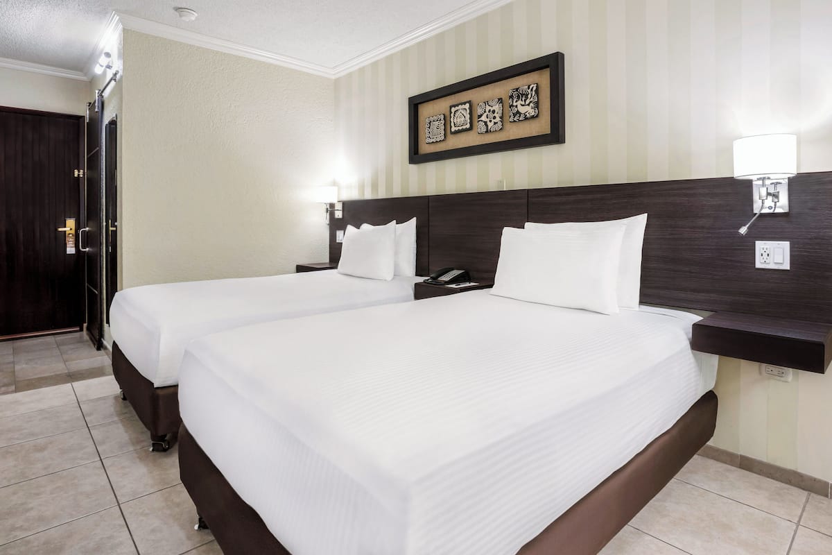 A hotel room with two beds, a dark wood headboard, a wall-mounted light, and a framed picture above the beds.
