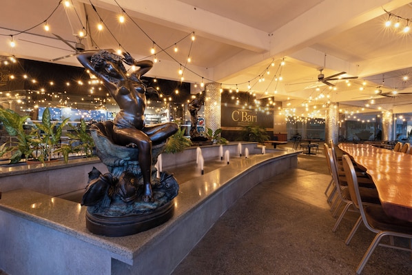 A modern hotel lobby with a central fountain, seating area, and string lights.