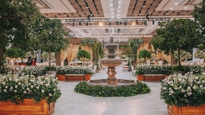 A spacious indoor garden with a central fountain, surrounded by wooden planters with white flowers. - Copantl Hotel & Convention Center (San Pedro Sula)