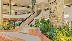A spacious lobby with a grand staircase, a large stone sculpture, and lush indoor plants. - Copantl Hotel & Convention Center (San Pedro Sula)