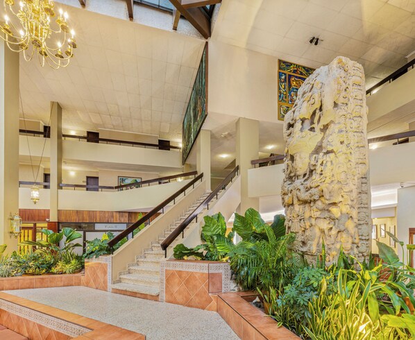 A spacious lobby with a grand staircase, a large stone sculpture, and lush indoor plants. - Copantl Hotel & Convention Center (San Pedro Sula)