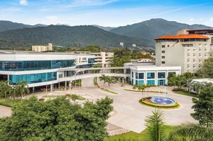 Un edificio moderno con fachada de vidrio, un patio central con una fuente y montañas al fondo.