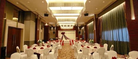 A banquet hall with round tables set for a formal event, featuring white tablecloths, red napkins, and floral centerpieces.
