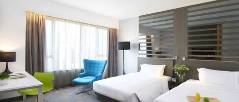 Habitación de hotel con dos camas, un escritorio con silla, una lámpara y una ventana con cortinas.