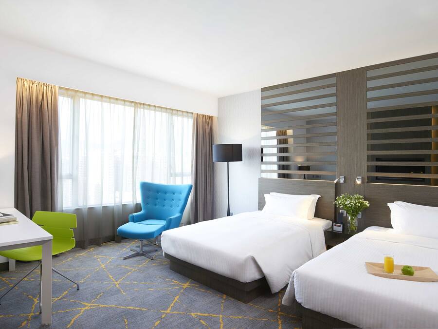 Une chambre d’hôtel avec deux lits, un bureau avec une chaise, une lampe et une fenêtre avec des rideaux.