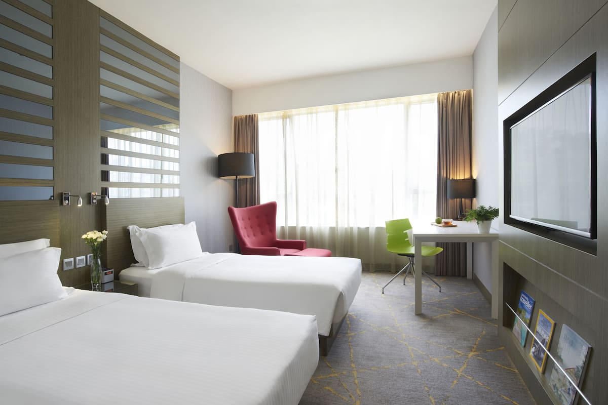 A hotel room with two beds, a desk, a TV, and a window with curtains.