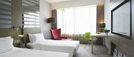 A hotel room with two beds, a desk, a TV, and a window with curtains.