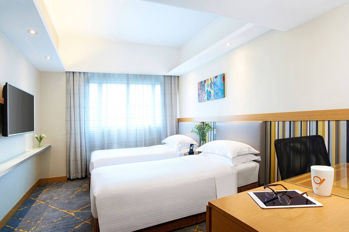 A hotel room with two beds, a desk with a chair, a television, and a window with curtains.