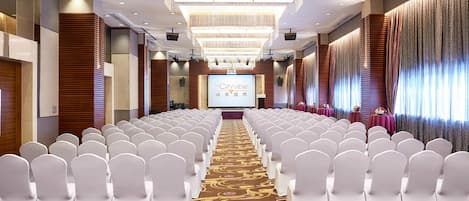 A conference room with rows of white chairs, a large screen at the front, and a patterned carpet.