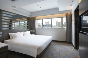 Una habitación de hotel moderna con una cama grande, televisión, vista a la ciudad y cortinas.