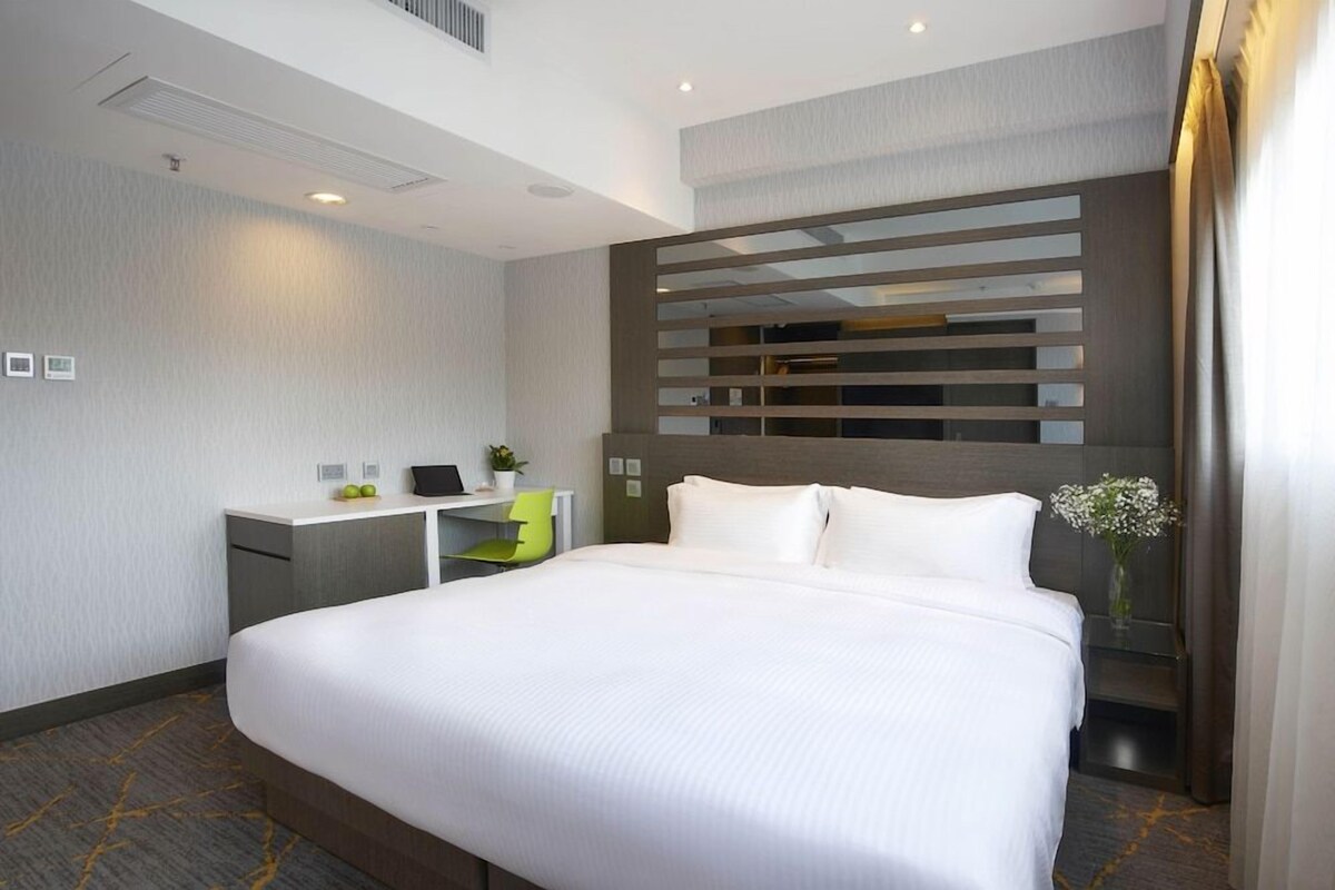 Habitación de hotel con una cama grande, un escritorio, una silla, una mesita con una planta y un panel decorativo en la pared.