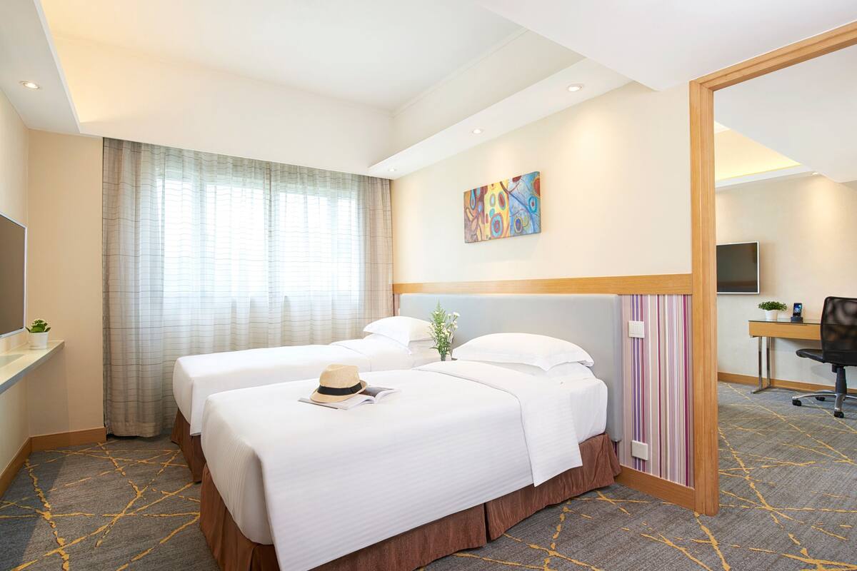 A hotel room with two beds, a desk, a TV, and a large mirror.