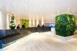A modern reception area with a curved marble counter, a green vertical garden, and a ceiling with circular lighting.