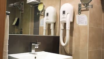 Un baño con un espejo grande, un lavabo y dos secadores de pelo fijados en la pared.