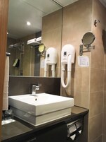 Un baño con un espejo grande, un lavabo y dos secadores de pelo fijados en la pared.