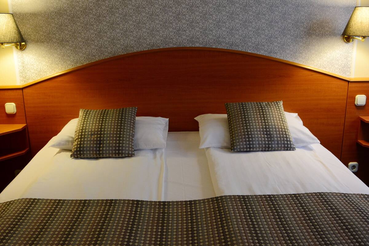 Una cama doble con dos almohadas, un cabecero de madera y dos lámparas de noche.