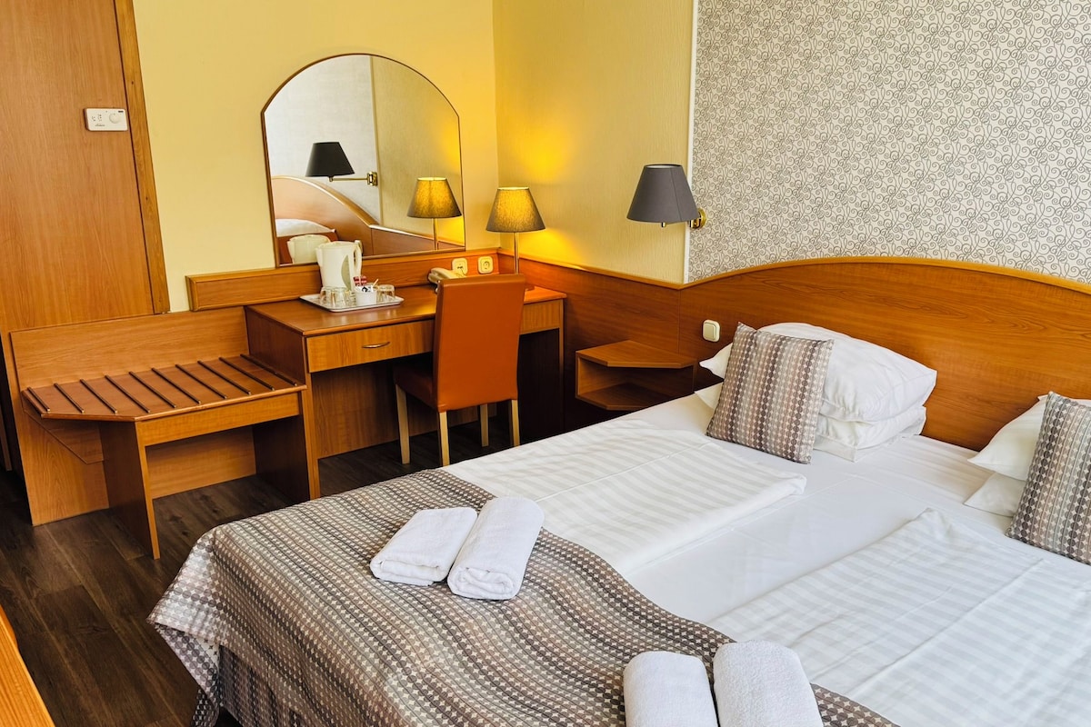 A hotel room with a bed, bedside table, desk, chair, and a mirror.