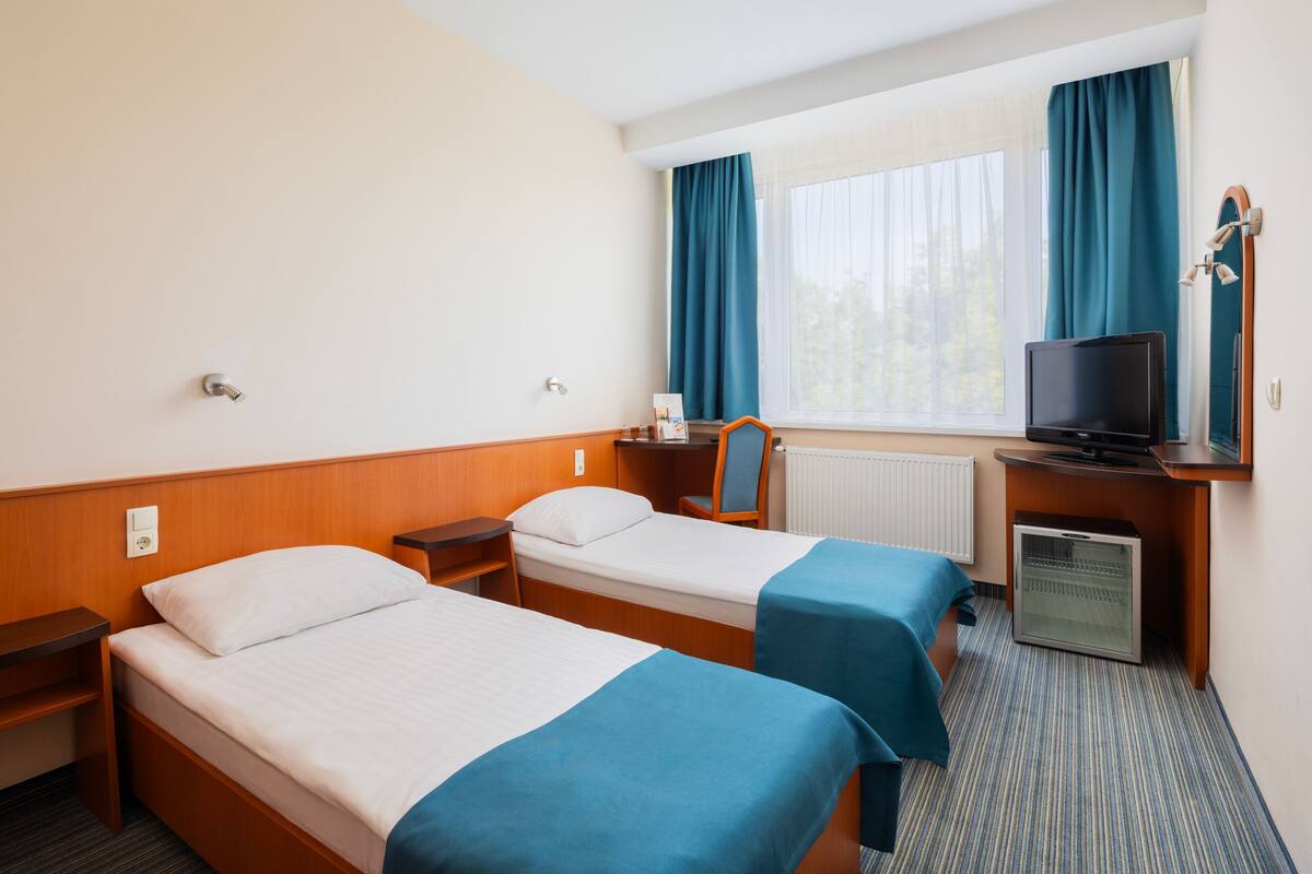 Une chambre d’hôtel avec deux lits, une télévision, un bureau avec un ordinateur et une fenêtre avec des rideaux.