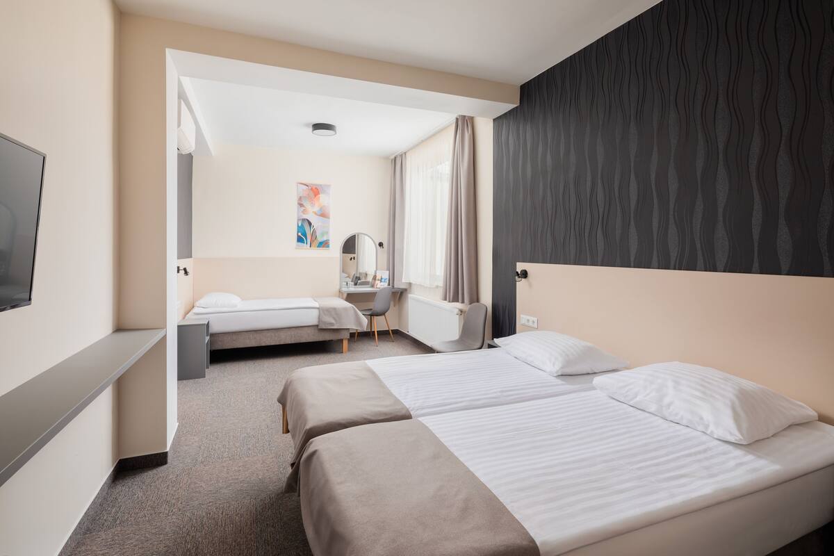 Une chambre d’hôtel avec deux lits, un bureau, une chaise, une télévision et une fenêtre avec des rideaux.