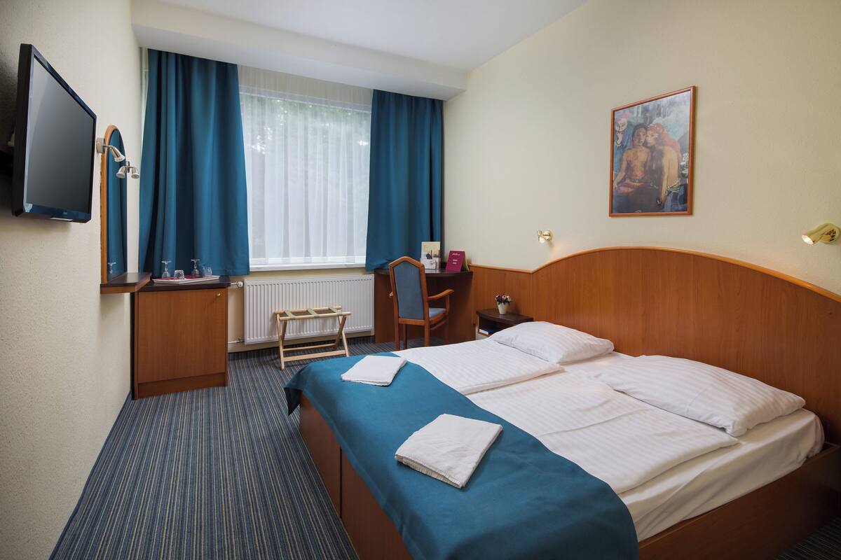 Une chambre d’hôtel avec un lit, un bureau et une chaise, une télévision et une fenêtre avec des rideaux.