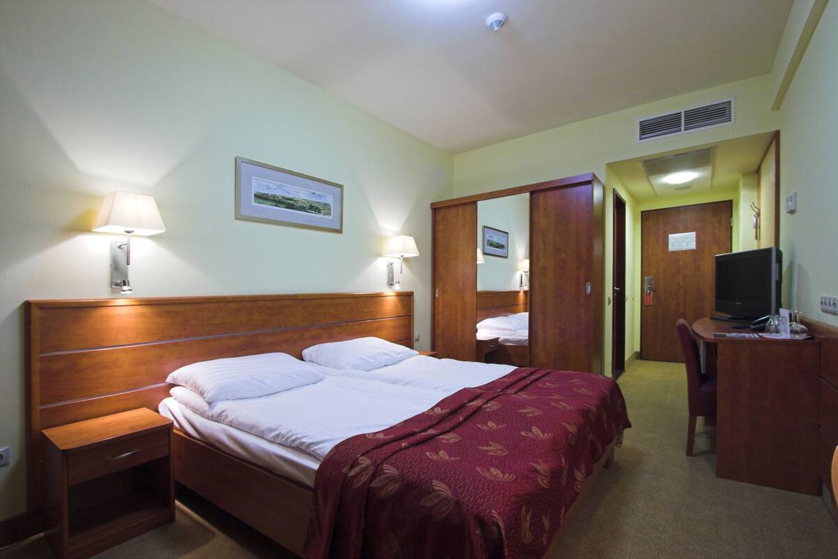 Une chambre d’hôtel avec un lit en bois, des lampes de chevet, un bureau avec un ordinateur et une télévision.