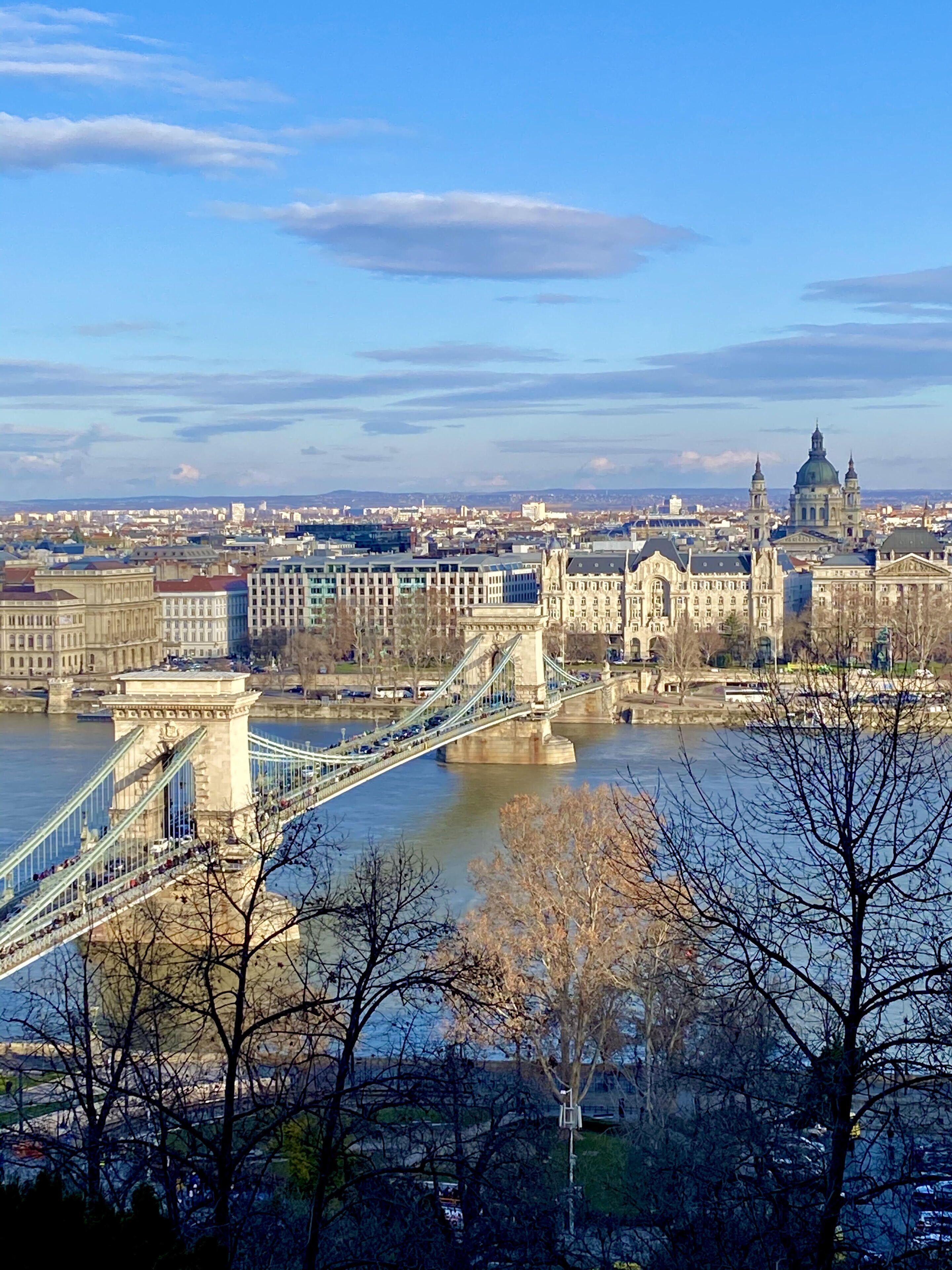 Μια πανοραμική θέα μιας πόλης με μια επιβλητική γέφυρα που διασχίζει ένα ποτάμι, ιστορικά κτίρια και έναν καθαρό ουρανό.