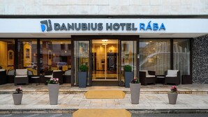 The exterior of Danubius Hotel Rába with a modern entrance, outdoor seating area, and potted plants. - Danubius Hotel Rába (Gyor)