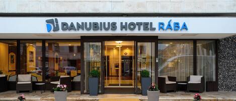 The exterior of Danubius Hotel Rába with a modern entrance, outdoor seating area, and potted plants.