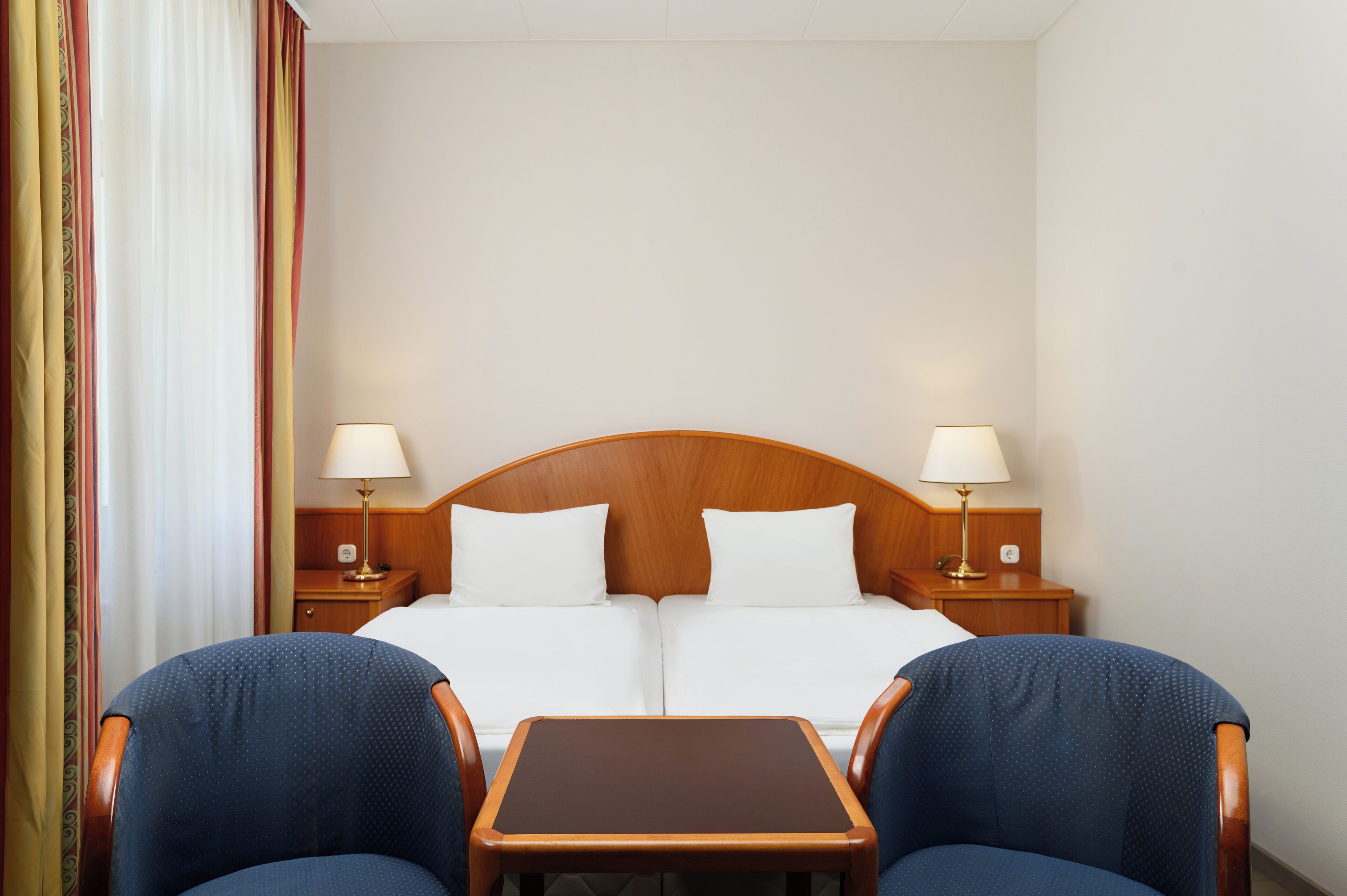 A hotel room with a double bed, two bedside tables with lamps, a small wooden table, and two armchairs.