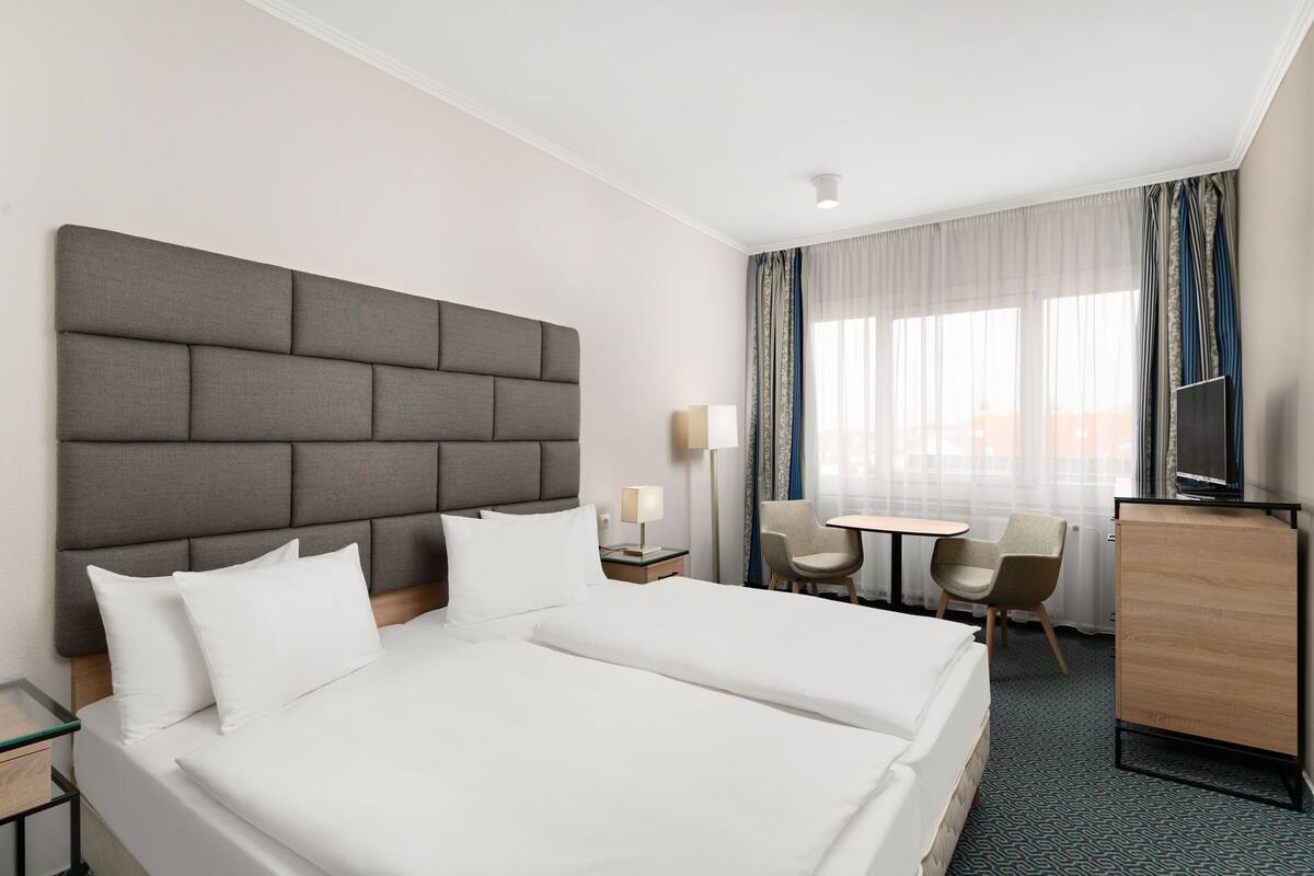 Habitación de hotel con una cama grande, un escritorio, dos sillas, un televisor y un armario.