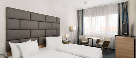A hotel room with a large bed, a desk, two chairs, a TV, and a wardrobe.
