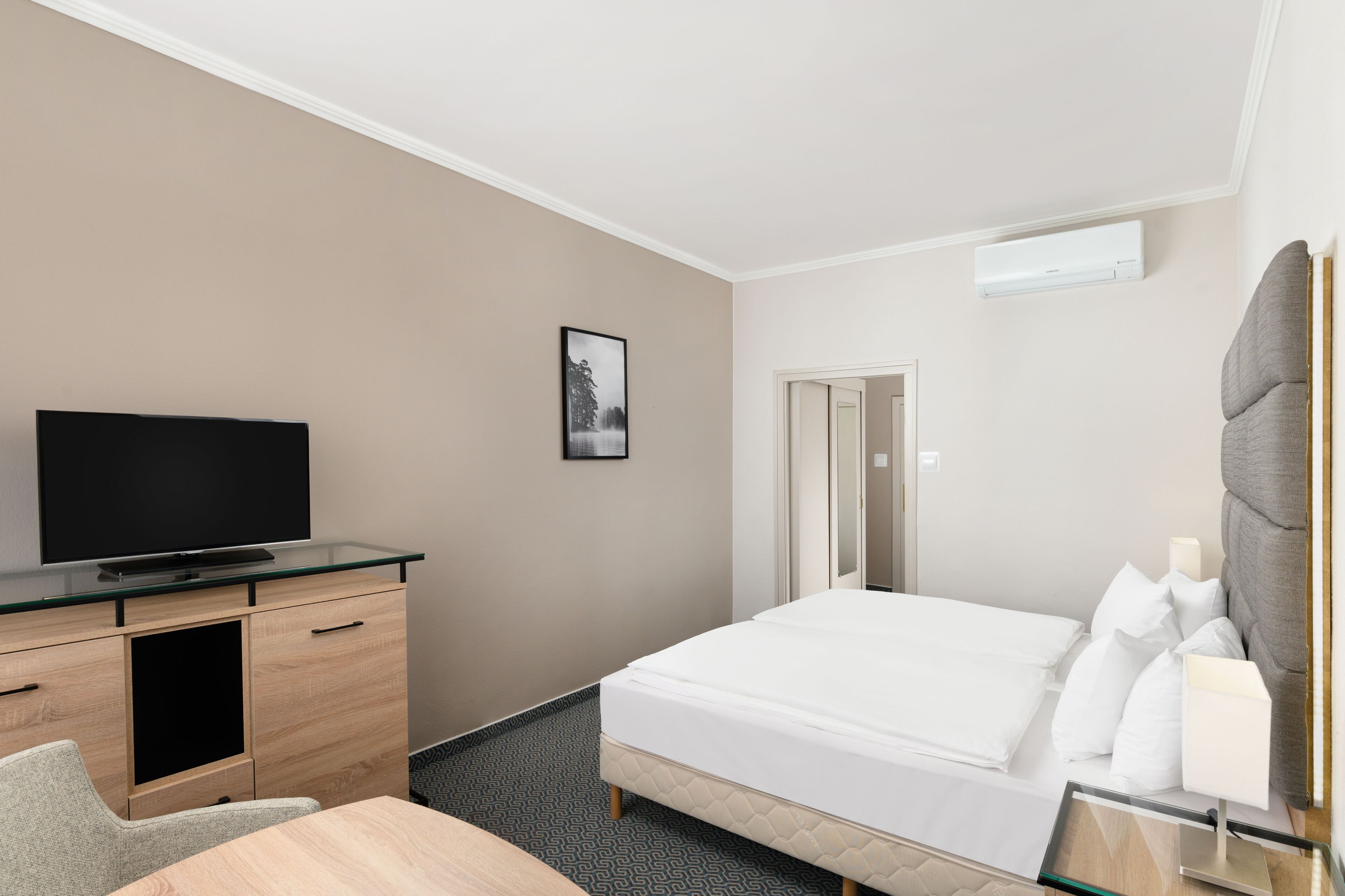 Een hotelkamer met een bed, een televisie op een houten dressoir, een bureau met een stoel en een deur naar de badkamer.