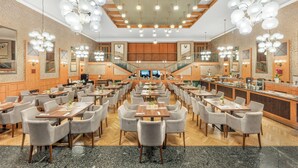 A spacious dining area with multiple tables and chairs, a central staircase, and a kitchen area visible in the background. - Danubius Hotel Rába (Gyor)