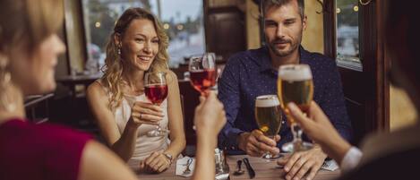 Un groupe de personnes est assis à une table dans un restaurant, d’où l’on peut admirer la vue sur la ville grâce à de grandes fenêtres.